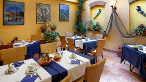 Un restaurante con mesas dispuestas para comer, destacando una pared amarilla con detalles decorativos y cuadros enmarcados.