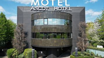 Un edificio moderno con facciata curva e ampie finestre, con la scritta 'Motel Ascot Hotel'.
