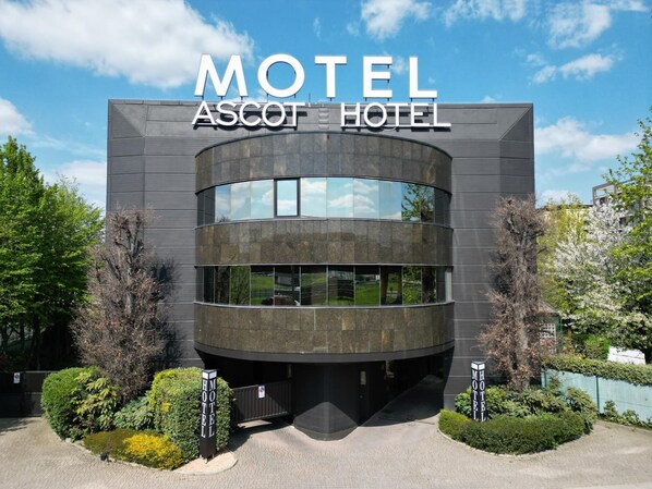 Un edificio moderno con fachada curva y ventanas amplias, identificado como 'Motel Ascot Hotel'.