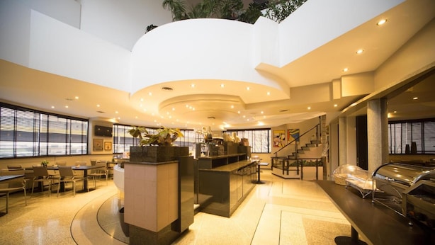 A hotel lobby with a central island, seating area, and a staircase leading to an upper level. - Hotel Motel Ascot (Lissone)