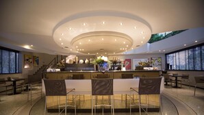 A modern hotel lobby with a central bar area, seating, and a staircase leading to an upper level. - Hotel Motel Ascot (Lissone)