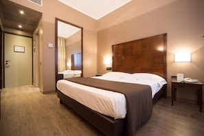 Ein Hotelzimmer mit einem großen Bett, einem hölzernen Kopfteil, einem Nachttisch mit Telefon und einem Spiegel an der Wand.
