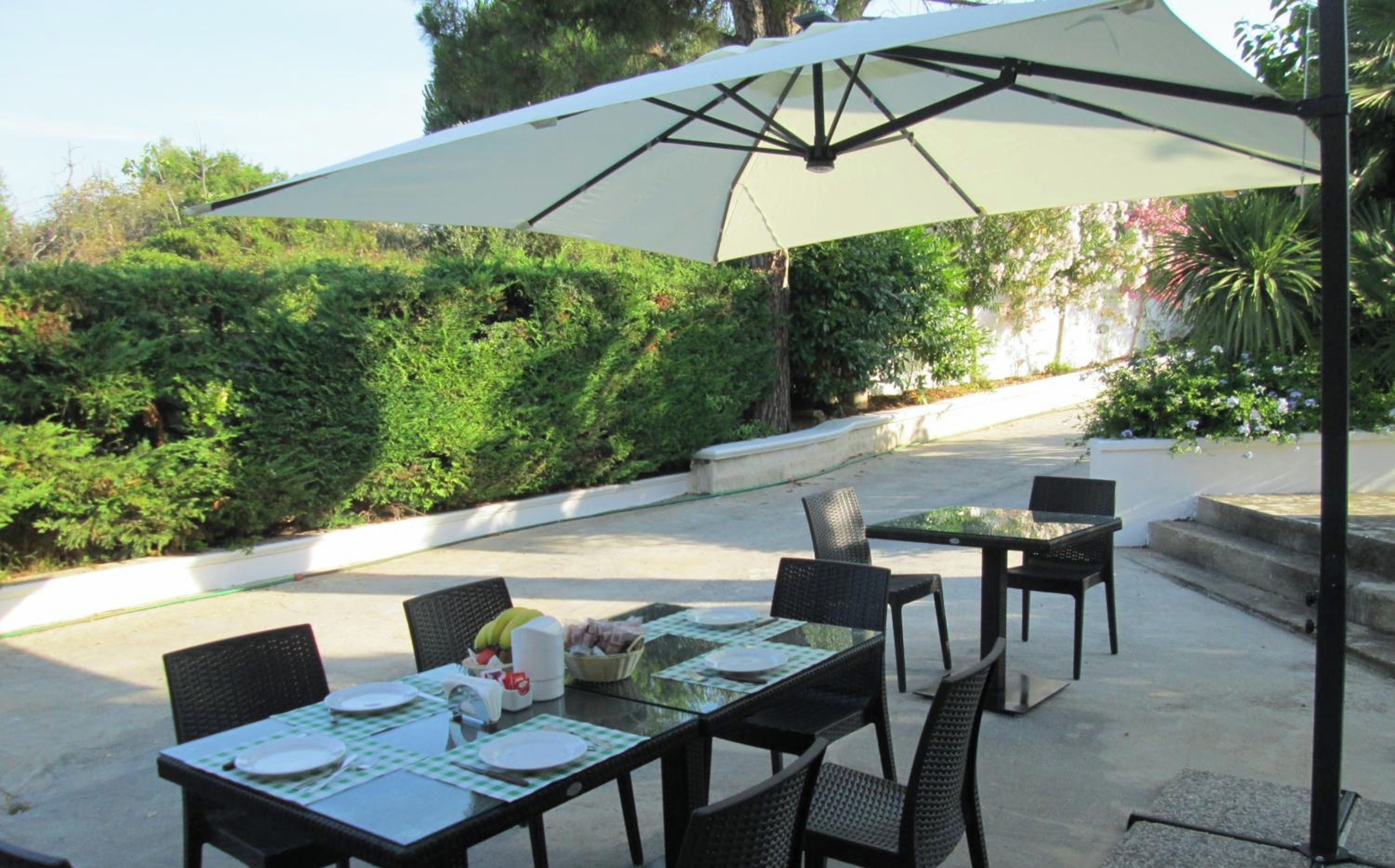 An outdoor patio with tables and chairs, surrounded by greenery.