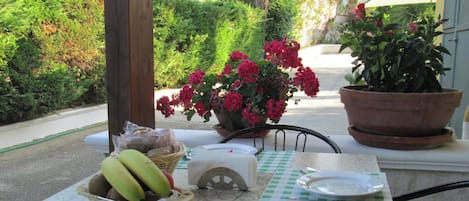 Una mesa con un cesto de plátanos, un objeto blanco pequeño, un plato de metal y un mantel a cuadros.
