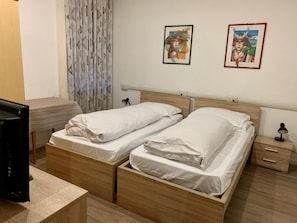 A hotel room with two single beds, a desk, a chair, a TV, and two framed pictures on the wall. - B&b Hotel Dolomiti (Bolzano)