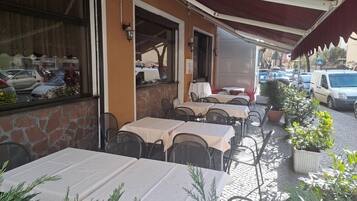 Un caffè all'aperto con tavoli e sedie, un muro in pietra e un'area coperta con un tendone rosso.