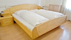 Una cama doble con estructura de madera y ropa de cama blanca, una mesita de noche con lámpara y un pequeño armario.