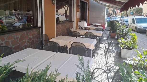 An outdoor cafe with tables and chairs, a stone wall, and a covered area with a red awning. - B&b Hotel Dolomiti (Bolzano)