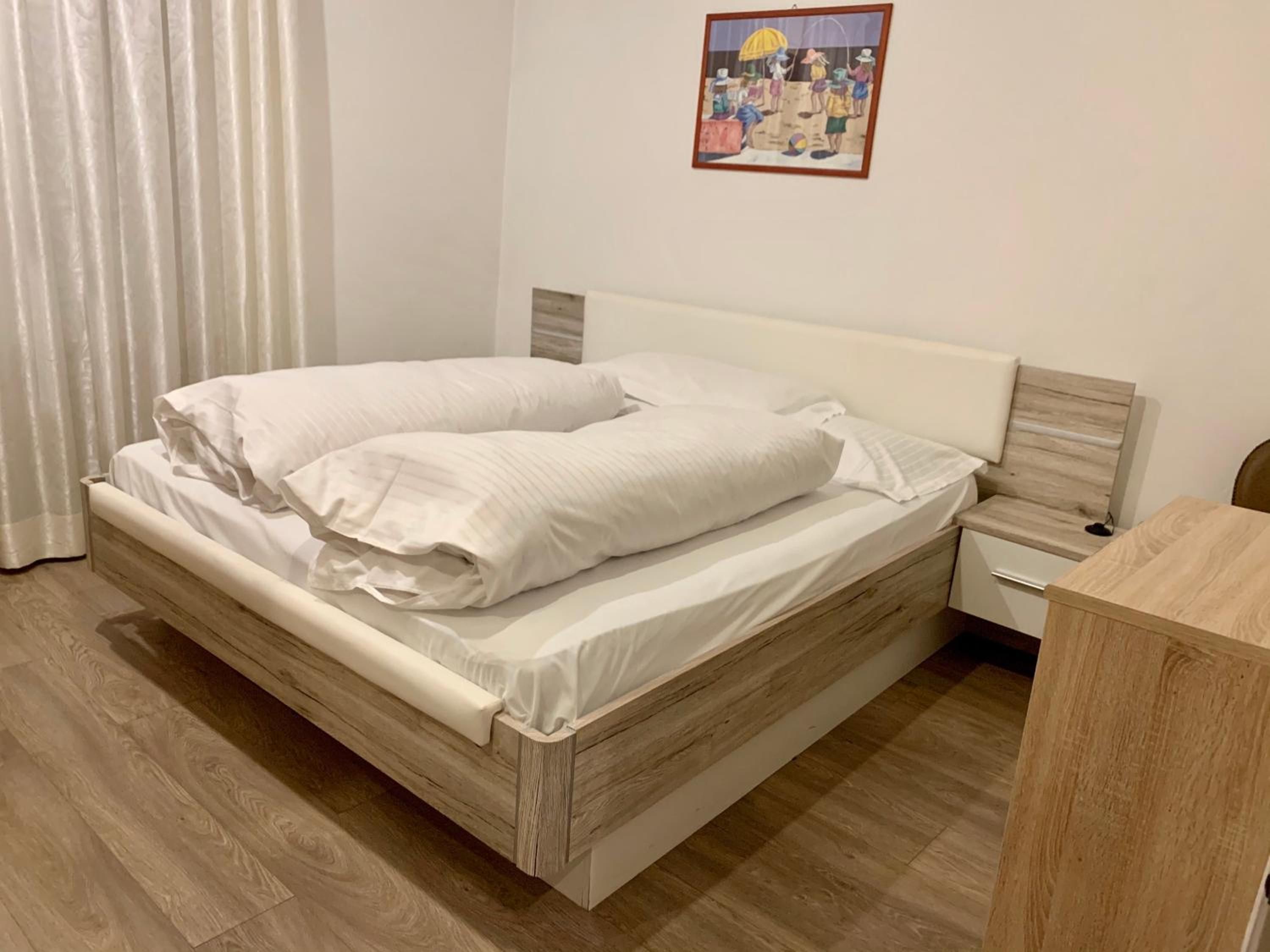 Una camera con un letto singolo, una testiera in legno, un comodino e un tavolino di servizio.