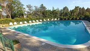 A swimming pool with a curved edge, surrounded by lounge chairs and greenery. - Park Hotel Galileo (Reggello)