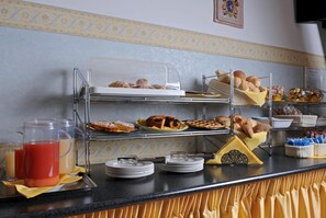 Un mostrador de buffet con varias estaciones de servicio, incluyendo pan, bollería y un dispensador de bebidas.