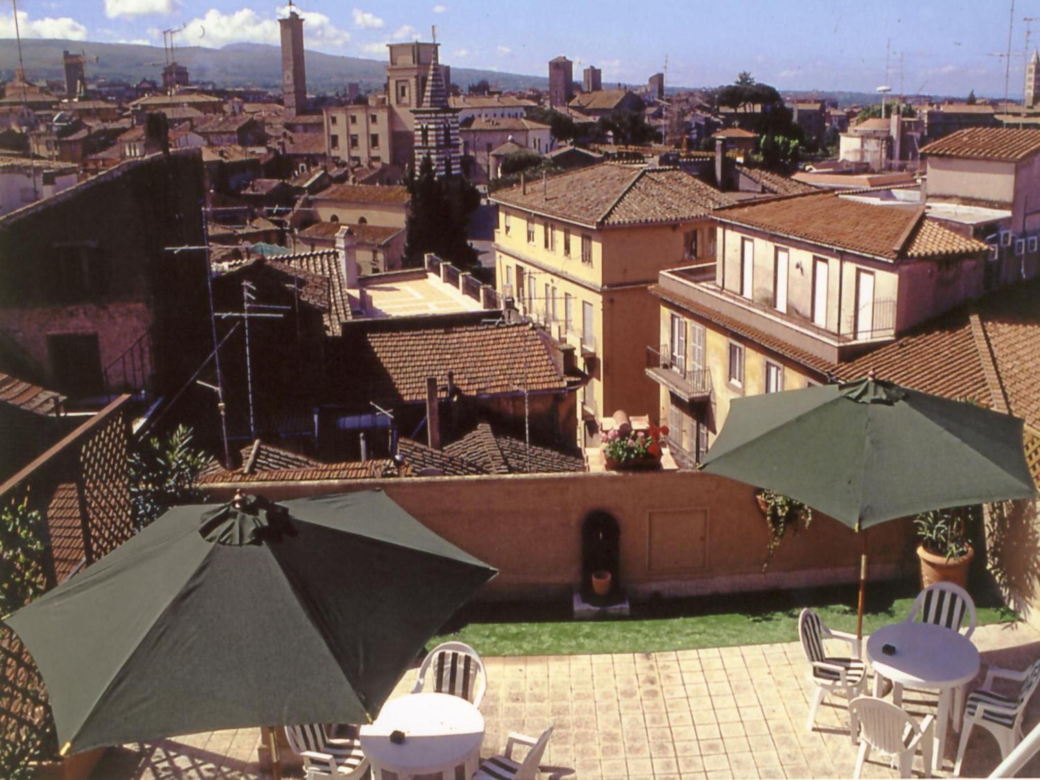 Un espace patio aménagé avec des sièges et des parasols, offrant une vue sur une ville historique dotée d’une architecture traditionnelle et d’un imposant beffroi.