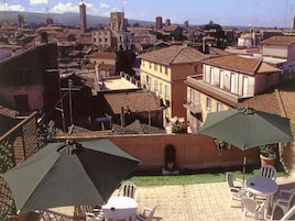 Un patio con mobiliario exterior y sombrillas, con vistas a un pueblo histórico de arquitectura tradicional y una torre destacada.