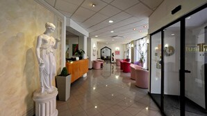 A reception area with a marble statue, a reception desk, and modern seating. - Tuscia Hotel (Viterbo)