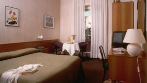 A hotel room with two beds, a desk with a lamp, a TV, and a window with curtains. - Tuscia Hotel (Viterbo)