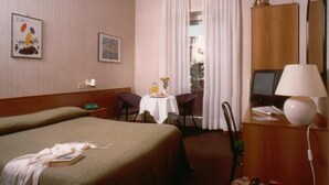 A hotel room with two beds, a desk with a lamp, a TV, and a window with curtains. - Tuscia Hotel (Viterbo)