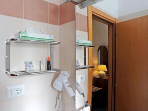 Un baño con secador de pelo, espejo y repisas con artículos de aseo.