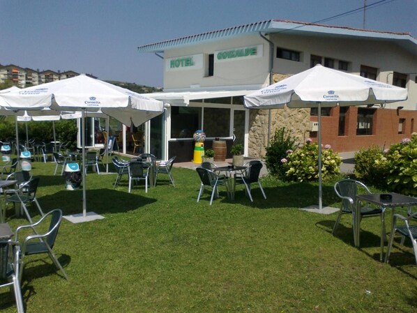 An outdoor seating area with tables and chairs, a covered patio, and a hotel building in the background.