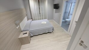 A hotel room with a bed, a TV mounted on the wall, a bathroom with a shower and toilet visible through an open door. - Hotel Goizalde (Sopelana)
