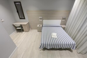 A bedroom with a bed, a desk, a chair, and a nightstand.