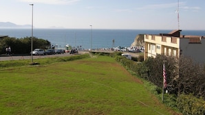 A coastal view with a grassy area, a road with parked cars, and buildings in the background. - Hotel Goizalde (Sopelana)