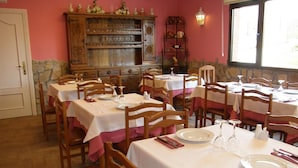 A dining area with multiple tables set for service, wooden chairs, and a decorative cabinet in the background. - Hotel Goizalde (Sopelana)