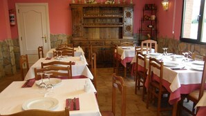 A dining area with multiple tables set for service, wooden chairs, a stone wall, and a wooden cabinet with glassware. - Hotel Goizalde (Sopelana)