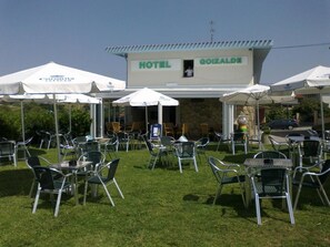 An outdoor seating area with tables and chairs, a sign for Hotel Goizalde, and umbrellas.