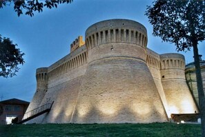 A large, historic stone fortress with a prominent central tower and a surrounding wall. - Locanda Le Logge (Urbisaglia)