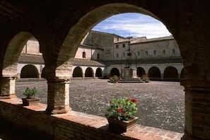 An open courtyard with arches, a fountain, and potted plants. - Locanda Le Logge (Urbisaglia)