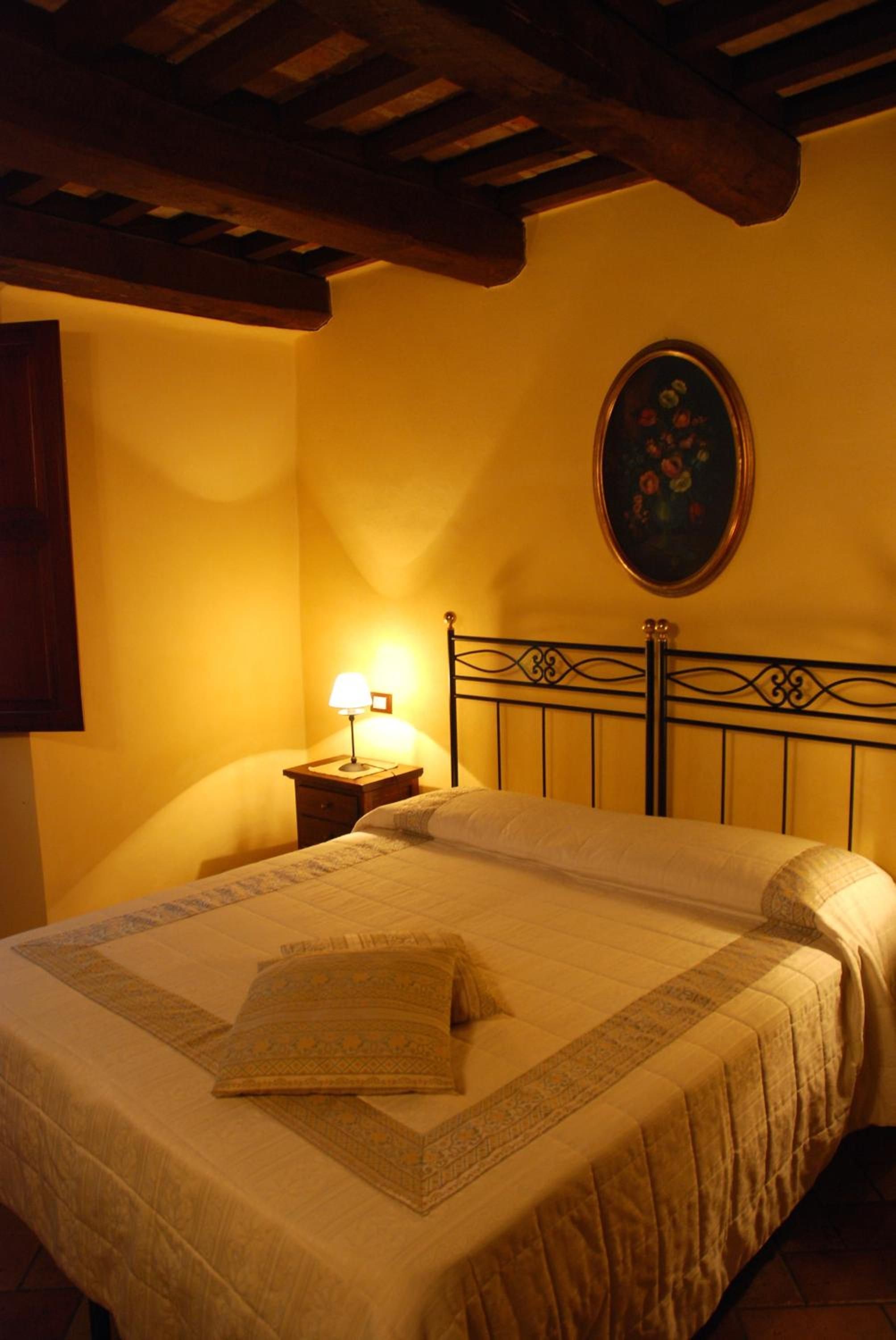 Una camera da letto con un letto, un comodino con una lampada, un quadro appeso al muro e un soffitto in legno.