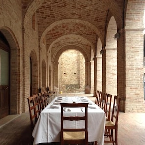 A long dining table with chairs, set in a brick-walled corridor with arched ceilings. - Locanda Le Logge (Urbisaglia)