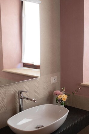 Un baño con un lavamanos blanco, un espejo y una ventana con cortina.