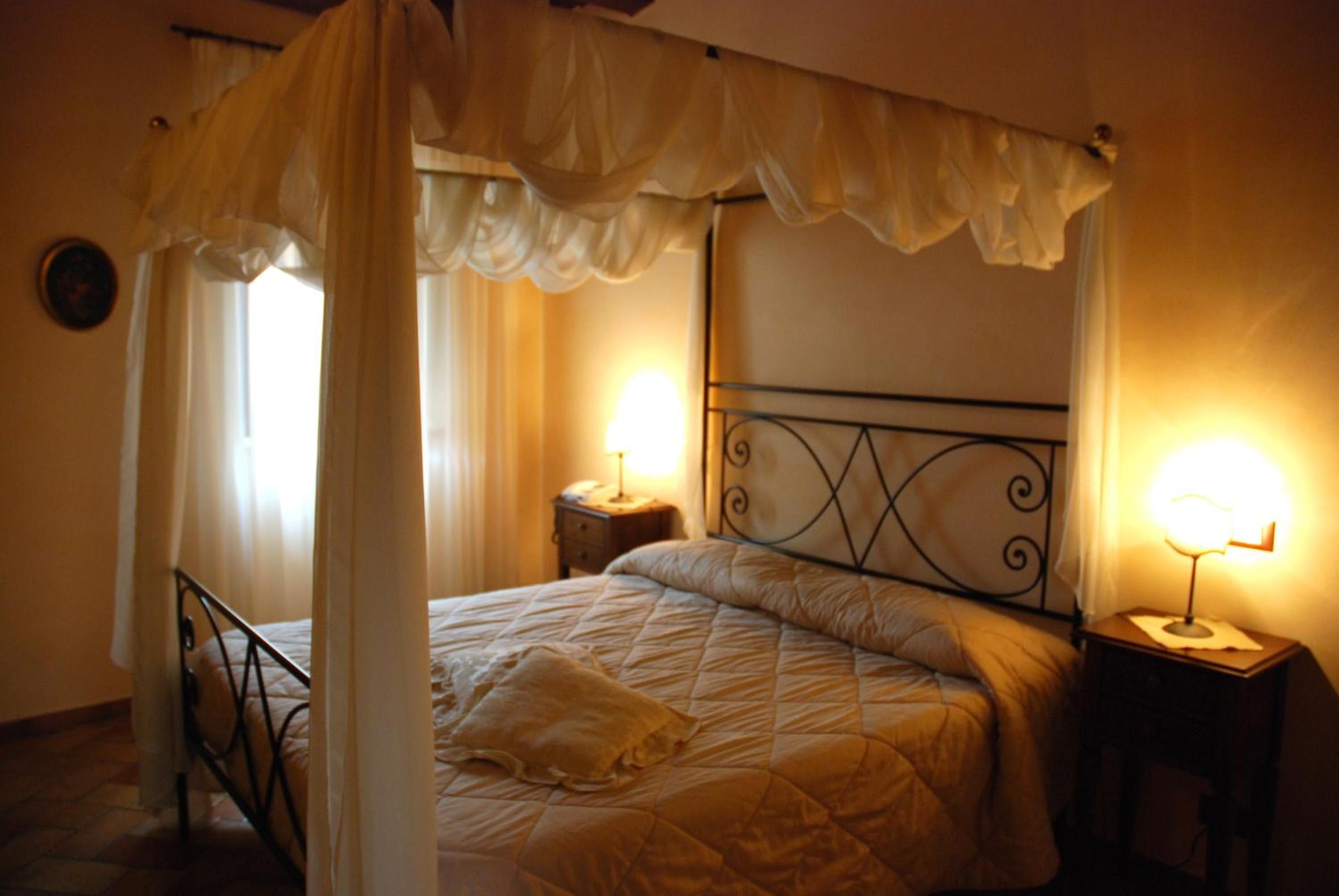 Una cama con dosel y cuatro columnas, con dos mesitas de noche, cada una con una lámpara.