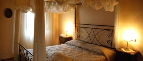 Una cama con dosel y cuatro columnas, con dos mesitas de noche, cada una con una lámpara.