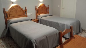 Et værelse med to senge med trægavl, hver med sengeborde og lamper. Der er en hvid dør og et lille bord i værelset.
