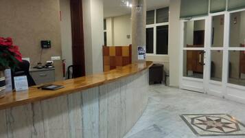 Zona de recepción con mostrador de mármol, detector de incendios, calendario y planta.