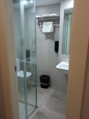 A bathroom with a glass shower enclosure, a toilet, a sink, and a trash bin. - Hotel Estrella Del Mar (Motril)