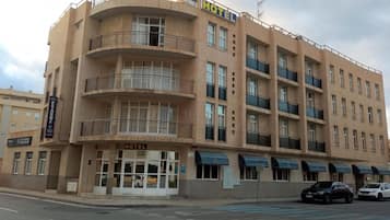Un hotel de varios pisos con balcones, un restaurante y un estacionamiento.
