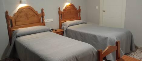 A room with two wooden beds, each with a headboard and bedside lamps. There is a white door and a small table in the room.
