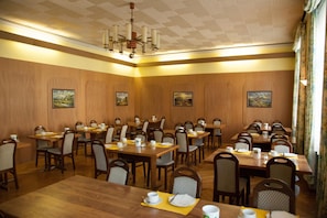 Un salón de conferencias con varias mesas y sillas, paredes de paneles de madera y decoración en el techo.
