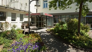 Un hotel llamado 'HOTEL TERMINUS' con una fachada moderna, zona de estar al aire libre y un jardín bien cuidado.