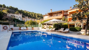A swimming pool with lounge chairs and umbrellas, surrounded by buildings and a hillside. - Hotel Robert (La Pobla de Claramunt)