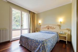 Habitación de hotel con una cama grande, una mesita de noche, una lámpara y vistas al exterior a través de una puerta corrediza.