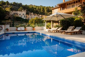 A swimming pool with lounge chairs and a pergola, surrounded by greenery and buildings in the background. - Hotel Robert (La Pobla de Claramunt)