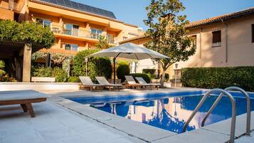 A swimming pool with lounge chairs and an umbrella, surrounded by buildings with solar panels.