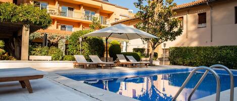 A swimming pool with lounge chairs and an umbrella, surrounded by buildings with solar panels.