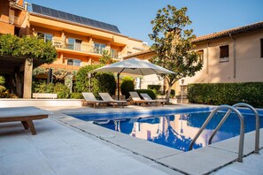 A swimming pool with lounge chairs and an umbrella, surrounded by buildings with solar panels. - Hotel Robert (La Pobla de Claramunt)