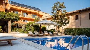 Ein Schwimmbecken mit Liegestühlen und Sonnenschirm, umgeben von Gebäuden mit Solaranlagen.