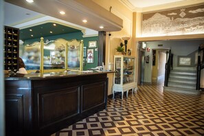Vestíbulo de hotel con mostrador de recepción, un mostrador de check-in, piso estampado y una escalera que lleva a otra zona.